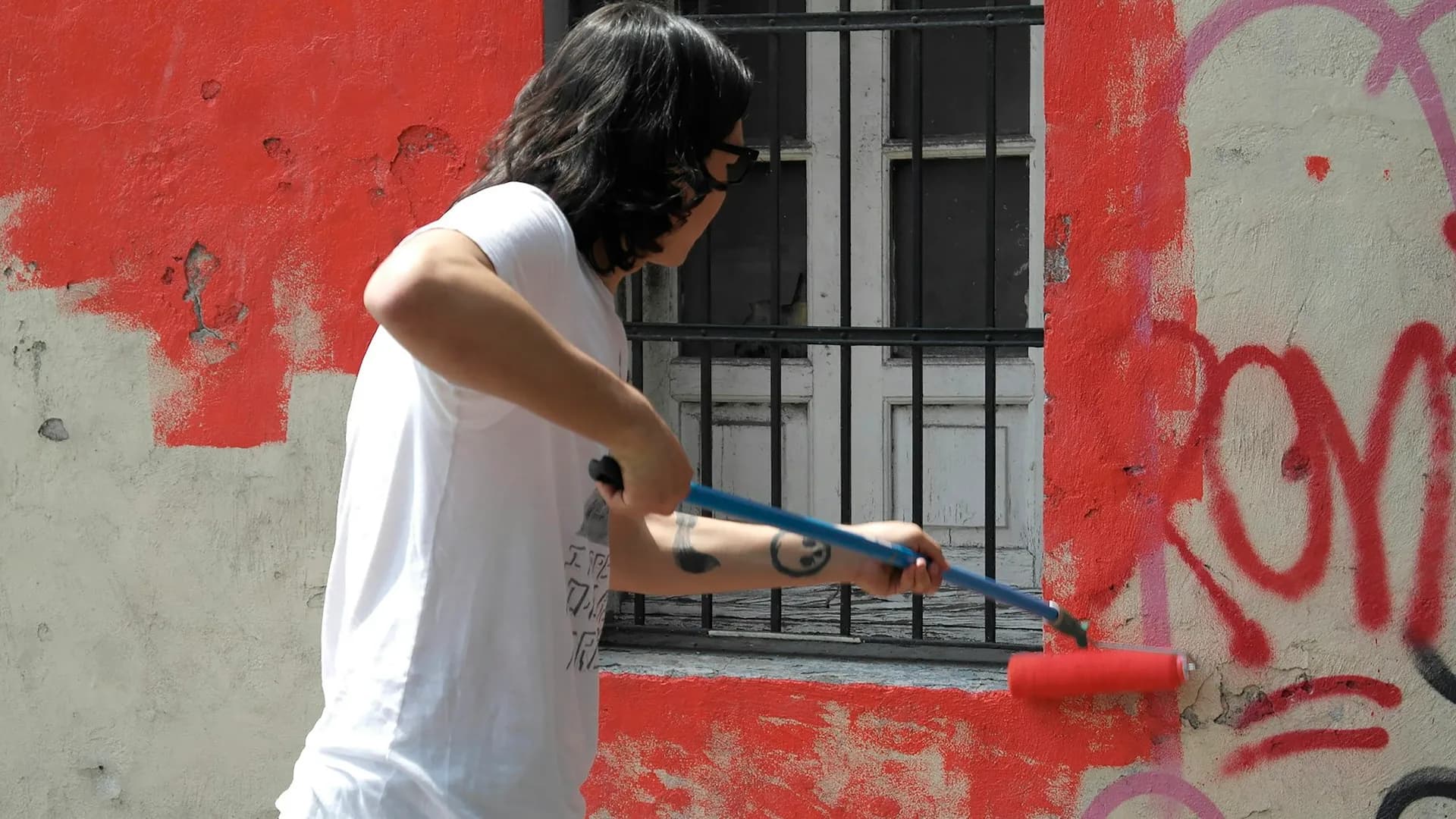 Pintor aplicando esmalte rojo sobre la fachada de una construcción